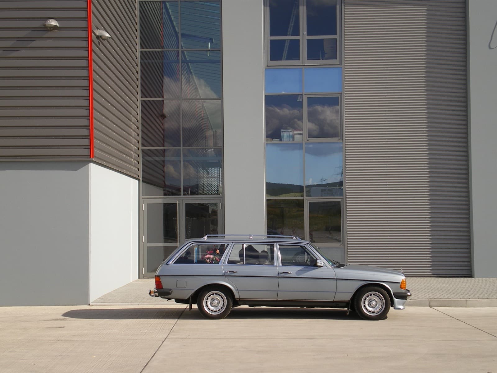 Graues W123 T-Modell vor einer modernen Glasfassade